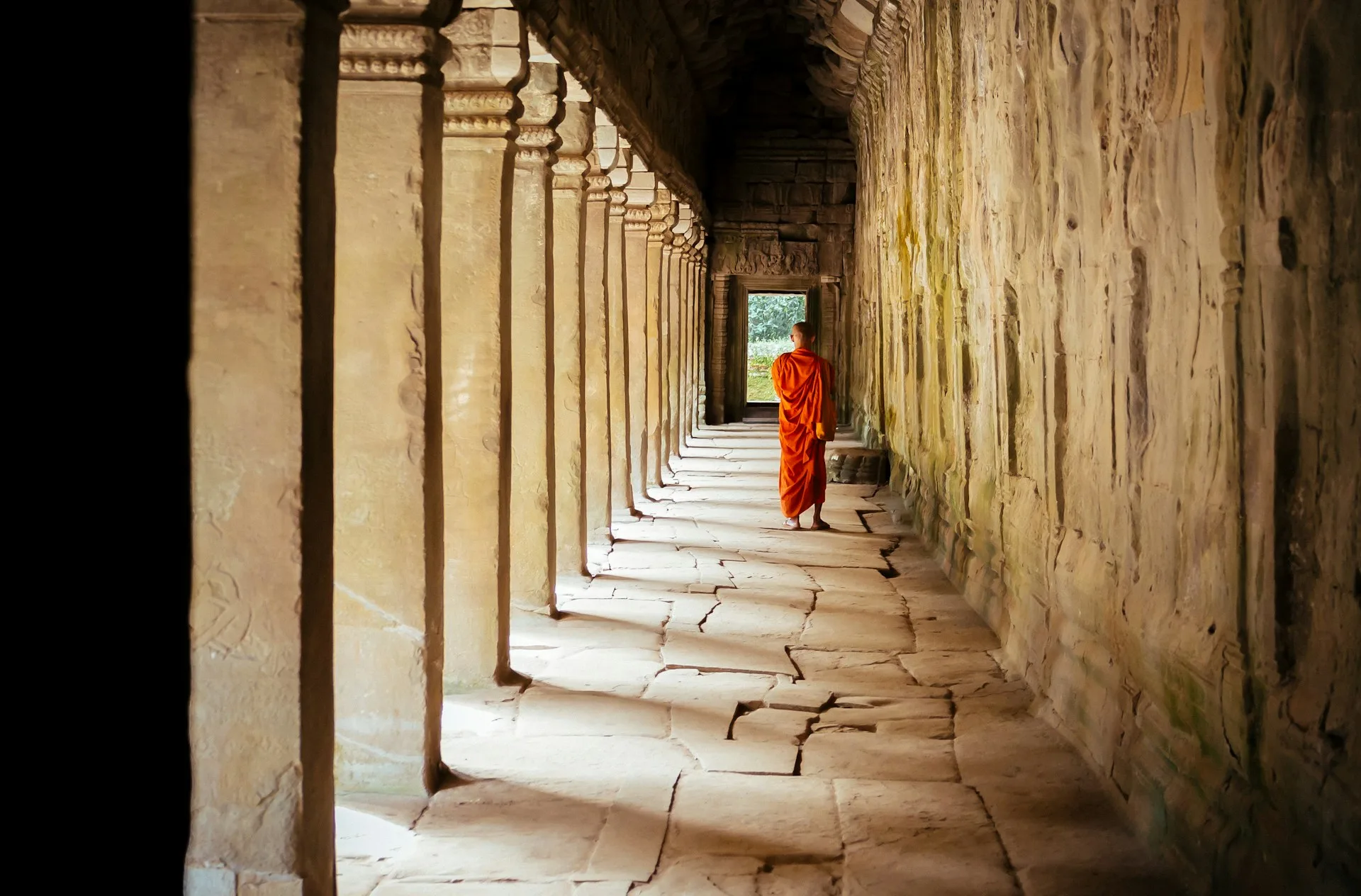Mnich w pomarańczowej szacie idący wzdłuż korytarza kolumnowego w starożytnej świątyni.