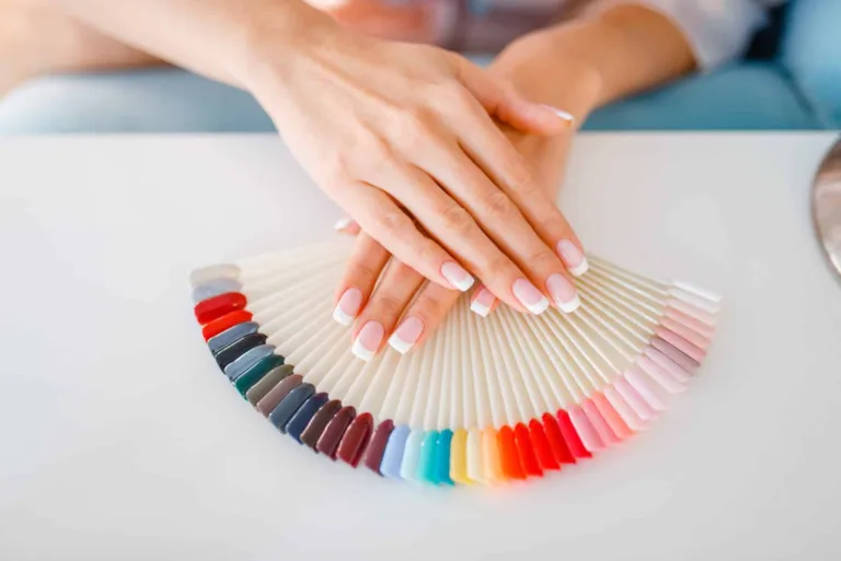 Dłonie kobiety z manicurem typu french położone na wzorniku z paletą kolorów lakierów do paznokci.