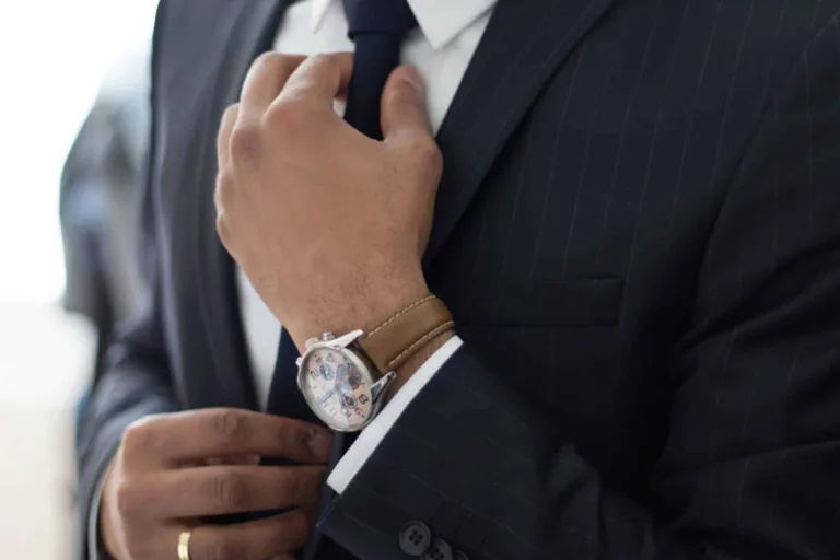 Mężczyzna w garniturze poprawiający krawat z zegarkiem na nadgarstku.