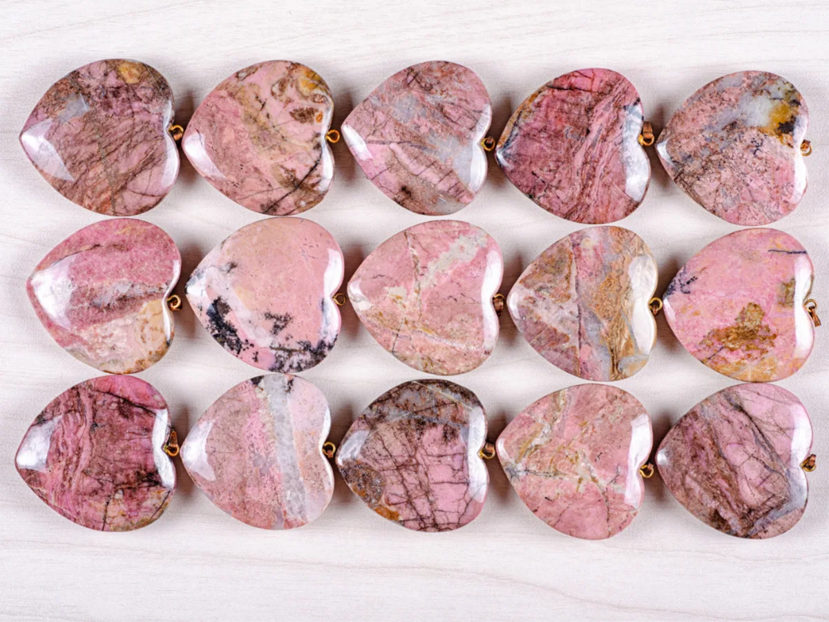Różowe kamienne rodonitu w kształcie serca ułożone w rzędach na jasnym tle.