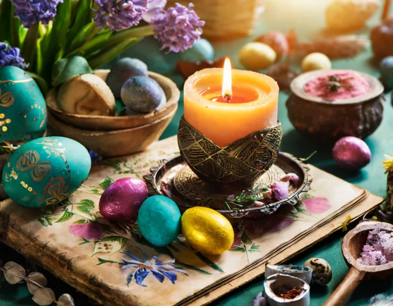 Stół z wielkanocnymi dekoracjami i symbolami ezoterycznymi, świecami, jajkami i kwiatami.