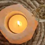 Świeca umieszczona w solnym świeczniku, obok suszonych kwiatów.